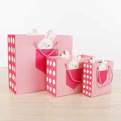 Geschenk-Einkaufstasche der Karikatur-Kindertages niedliches rosa Kaninchen, das Geschenkpapiertüte faltet